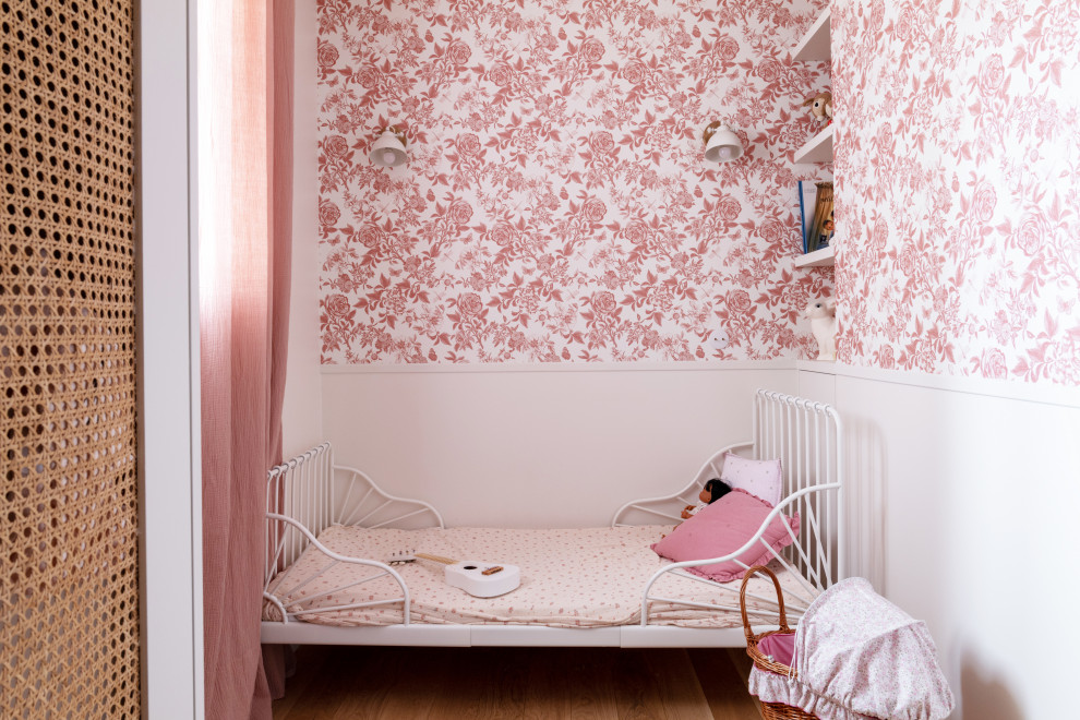 Modelo de dormitorio infantil de 1 a 3 años campestre pequeño con paredes rosas, suelo de madera clara, suelo beige y papel pintado