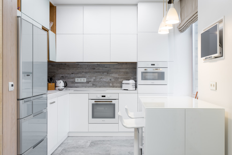 Mid-sized scandinavian l-shaped open plan kitchen in Moscow with flat-panel cabinets, white cabinets, grey splashback, porcelain splashback, white appliances, porcelain floors, a drop-in sink, solid surface benchtops, grey floor and white benchtop.