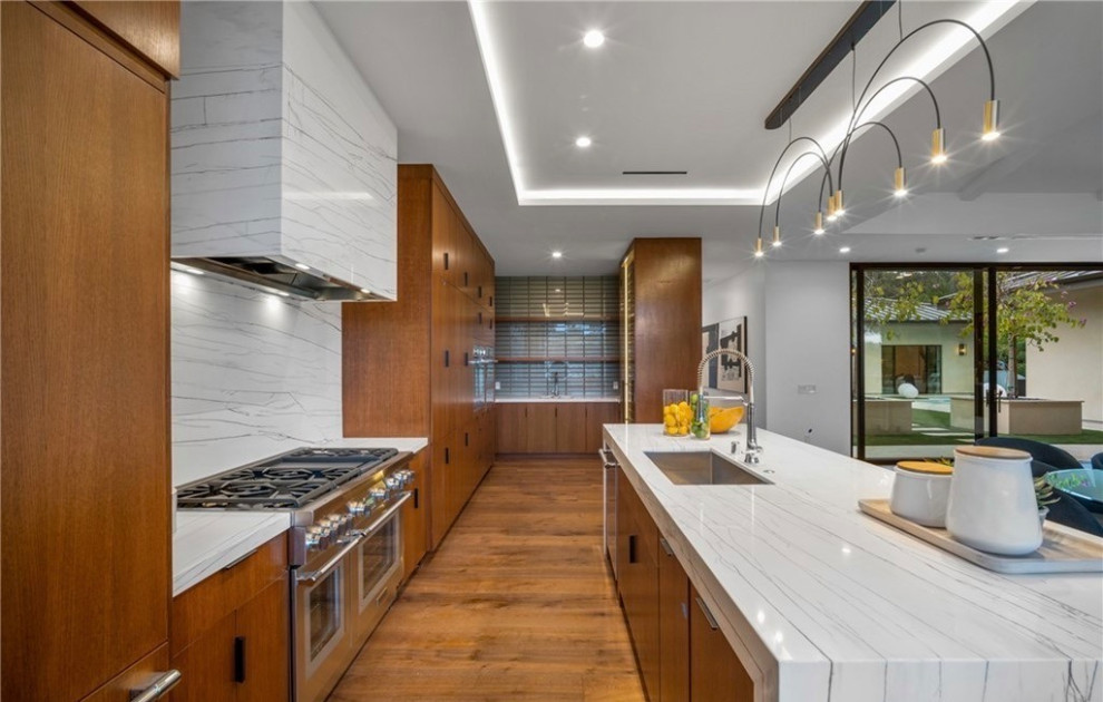 Design ideas for a contemporary open plan kitchen in Orange County with a belfast sink, flat-panel cabinets, dark wood cabinets, marble worktops, stainless steel appliances, medium hardwood flooring, an island, brown floors, white worktops and a drop ceiling.