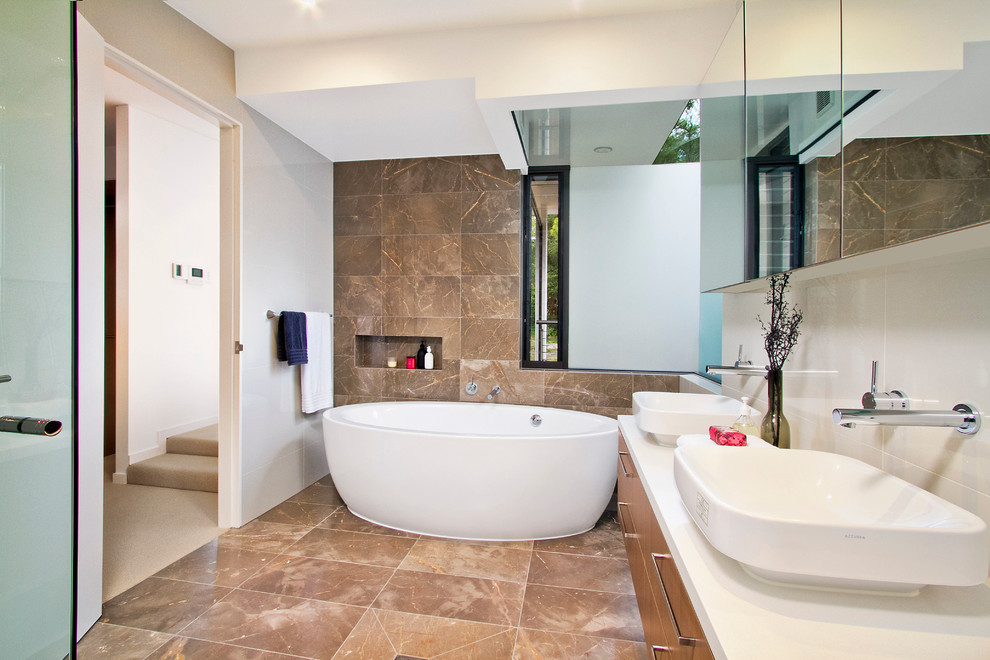This is an example of a contemporary master bathroom in Sydney with flat-panel cabinets, a vessel sink, medium wood cabinets, a freestanding tub, brown tile and grey walls.