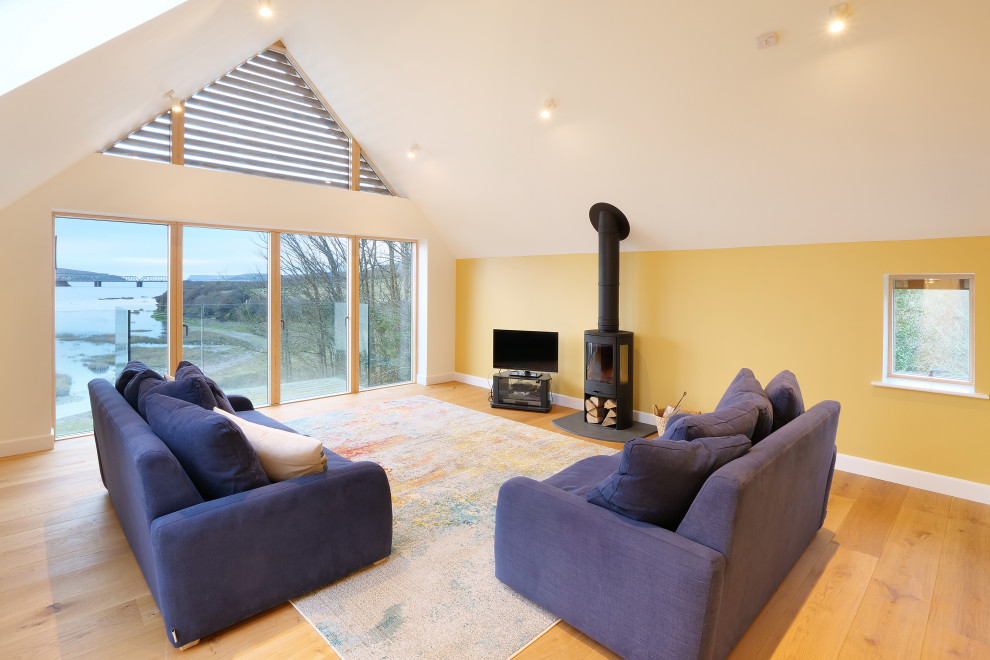 Mittelgroßes, Abgetrenntes Modernes Wohnzimmer mit gelber Wandfarbe, braunem Holzboden, Kaminofen, freistehendem TV und gewölbter Decke in Cornwall