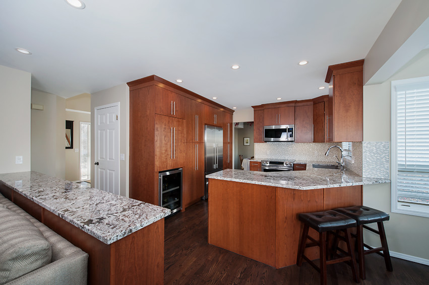Mid-sized transitional u-shaped dark wood floor open concept kitchen photo in Calgary with an undermount sink, flat-panel cabinets, medium tone wood cabinets, granite countertops, white backsplash, mirror backsplash, stainless steel appliances and an island