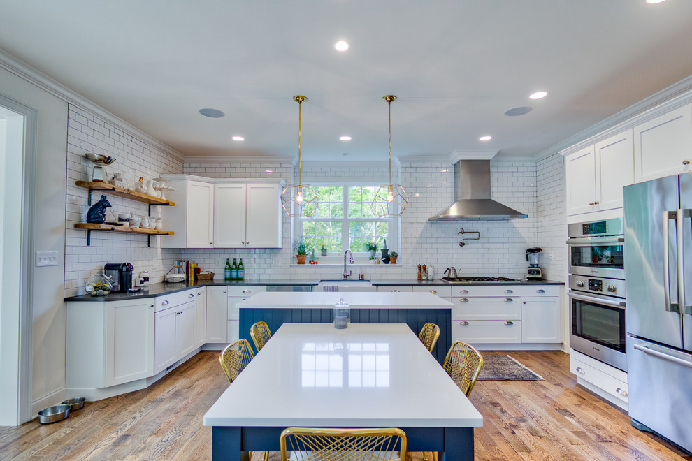 Design ideas for a transitional u-shaped eat-in kitchen in Philadelphia with a farmhouse sink, shaker cabinets, blue cabinets, white splashback, subway tile splashback, stainless steel appliances, medium hardwood floors, with island, brown floor and white benchtop.