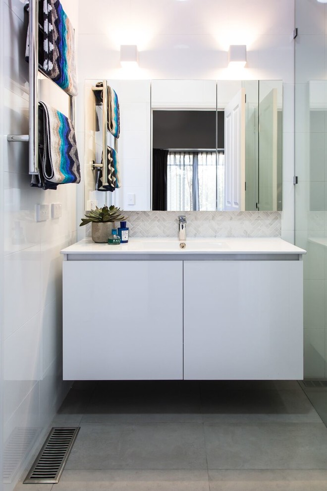 This is an example of a small contemporary bathroom in Melbourne with flat-panel cabinets, white cabinets, a curbless shower, a two-piece toilet, porcelain tile, white walls, porcelain floors, an integrated sink, solid surface benchtops, grey floor, a hinged shower door and white benchtops.