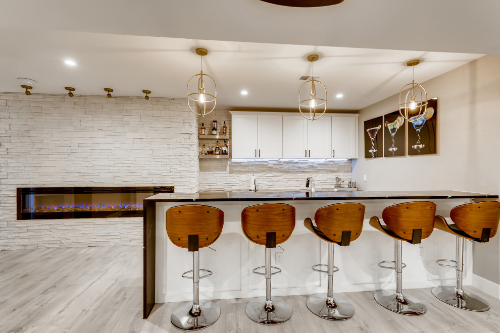 This is an example of a large modern galley wet bar in Denver with an undermount sink, recessed-panel cabinets, white cabinets, quartzite benchtops, white splashback, stone slab splashback, vinyl floors, grey floor and black benchtop.