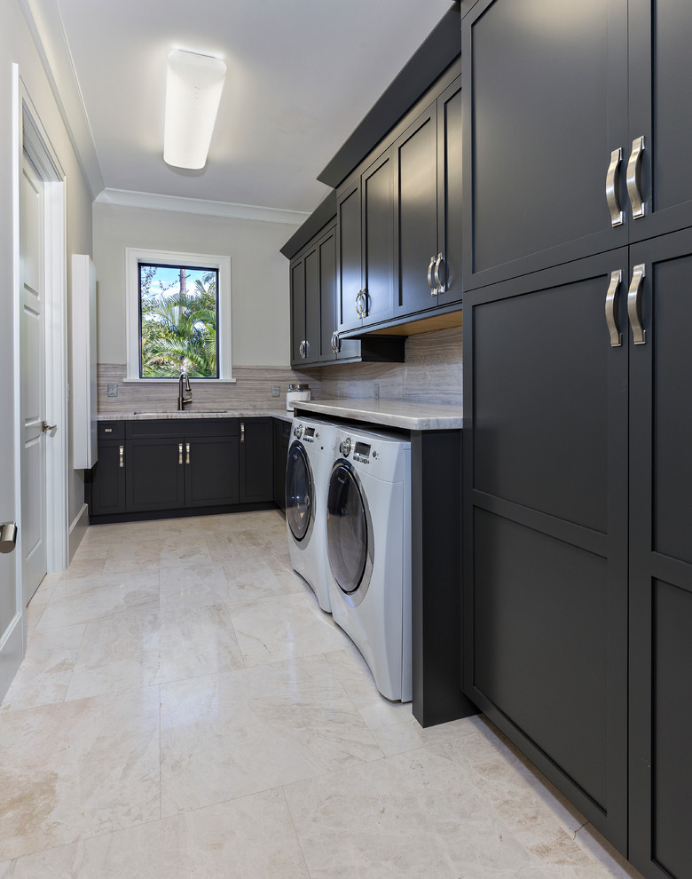 Photo of a large contemporary single-wall laundry room in Miami with an undermount sink, recessed-panel cabinets, black cabinets, marble benchtops, beige walls, marble floors and a side-by-side washer and dryer.