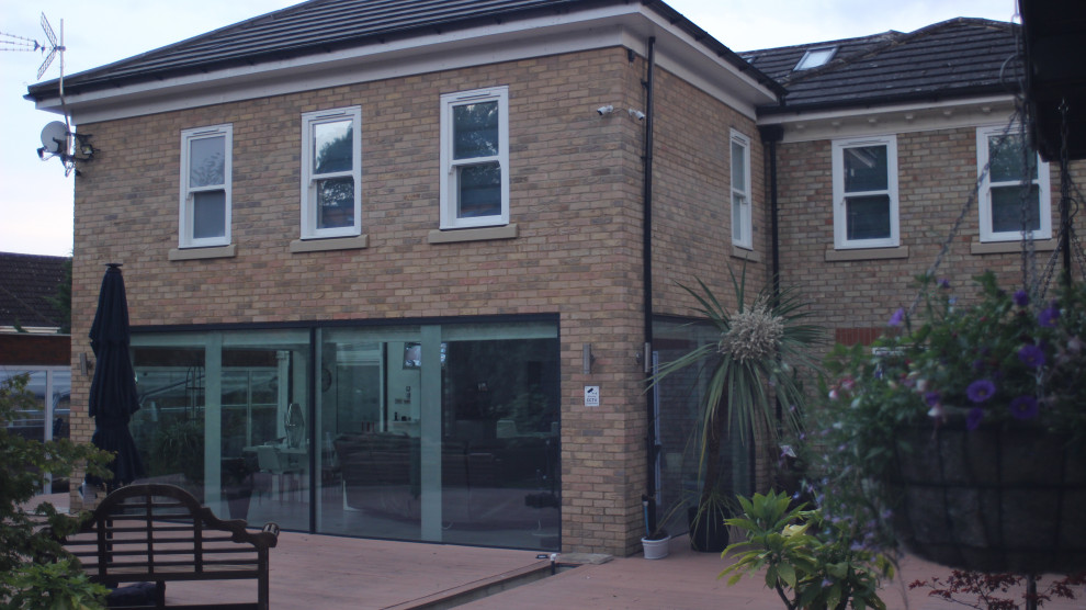 Photo of a mid-sized contemporary two-storey brick beige house exterior in Buckinghamshire with a gable roof, a tile roof and a black roof.
