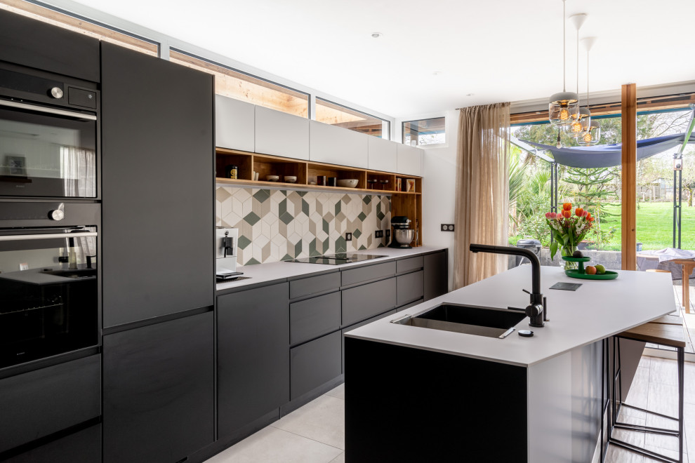 Cuisine ouverte?[Réalisation de cuisine ouverte With un évier encastré, un placard à porte plane, des portes de placard noires, un plan de travail en surface solide, une crédence multicolore, un électroménager noir, un sol en carrelage de céramique, îlot, un sol gris and un plan de travail blanc.]:[Réalisation de cuisines ouvertes With un évier encastré, un placard à porte plane, des portes de placard noires, un plan de travail en surface solide, une crédence multicolore, un électroménager noir, un sol en carrelage de céramique, îlot, un sol gris and un plan de travail blanc.]
