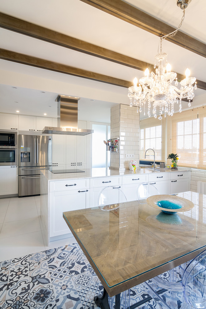 This is an example of a transitional eat-in kitchen in Madrid with shaker cabinets, white cabinets, stainless steel appliances, a peninsula, white benchtop and blue floor.