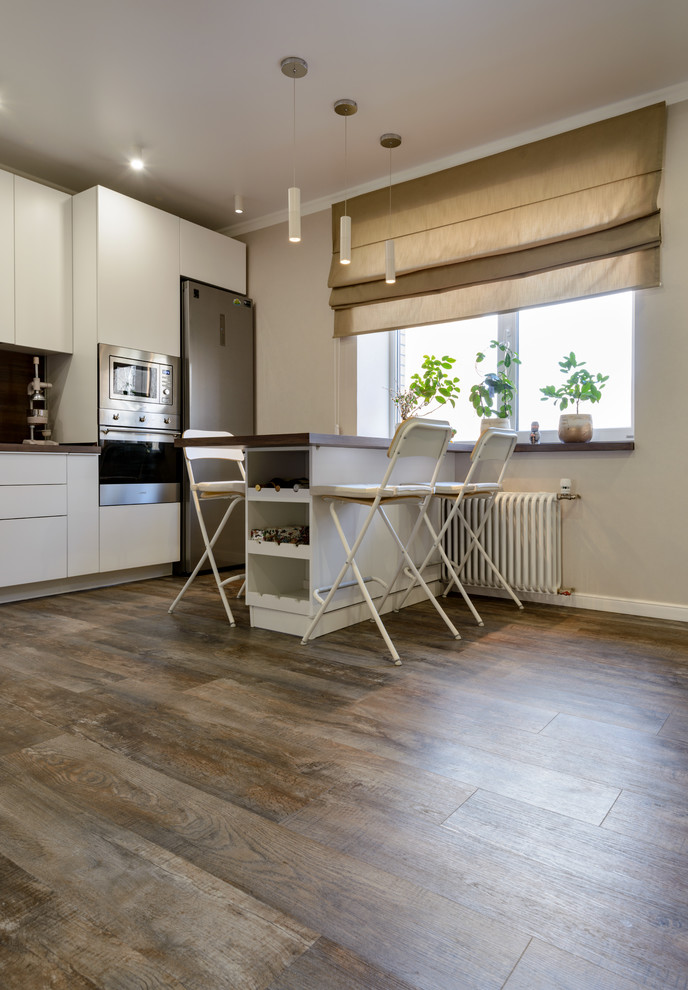 Large contemporary l-shaped open plan kitchen in Novosibirsk with a drop-in sink, flat-panel cabinets, white cabinets, wood benchtops, brown splashback, timber splashback, stainless steel appliances, vinyl floors, with island, brown floor and brown benchtop.