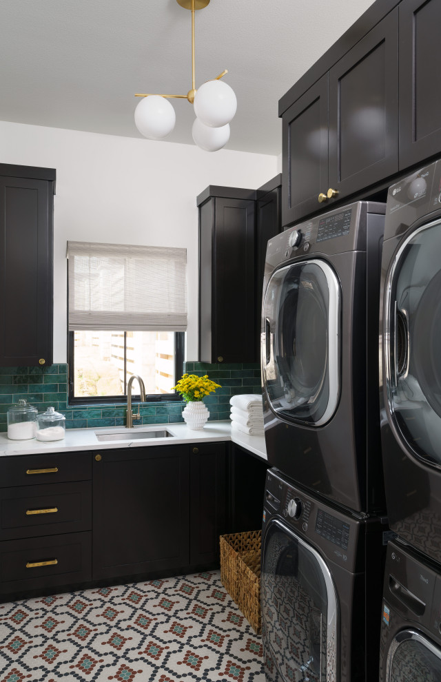 This is an example of a traditional l-shaped utility room in Austin with a submerged sink, shaker cabinets, black cabinets, green splashback, white walls, a stacked washer and dryer, multi-coloured floors and white worktops.