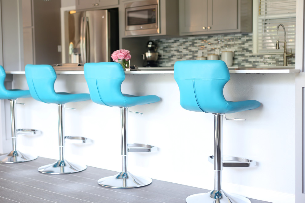 Example of a mid-sized transitional u-shaped porcelain tile and gray floor eat-in kitchen design with shaker cabinets, gray cabinets, glass sheet backsplash, stainless steel appliances, an island, a farmhouse sink, quartz countertops and blue backsplash