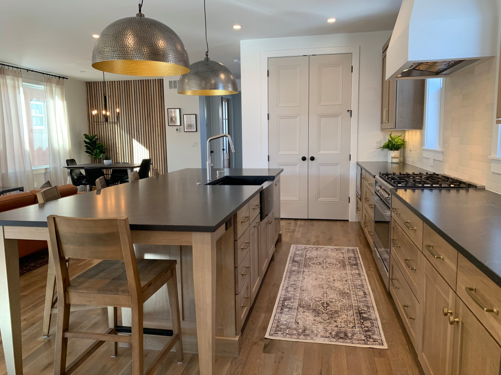 Transitional medium tone wood floor kitchen photo in Denver with shaker cabinets, medium tone wood cabinets, soapstone countertops, white backsplash, porcelain backsplash, stainless steel appliances and black countertops