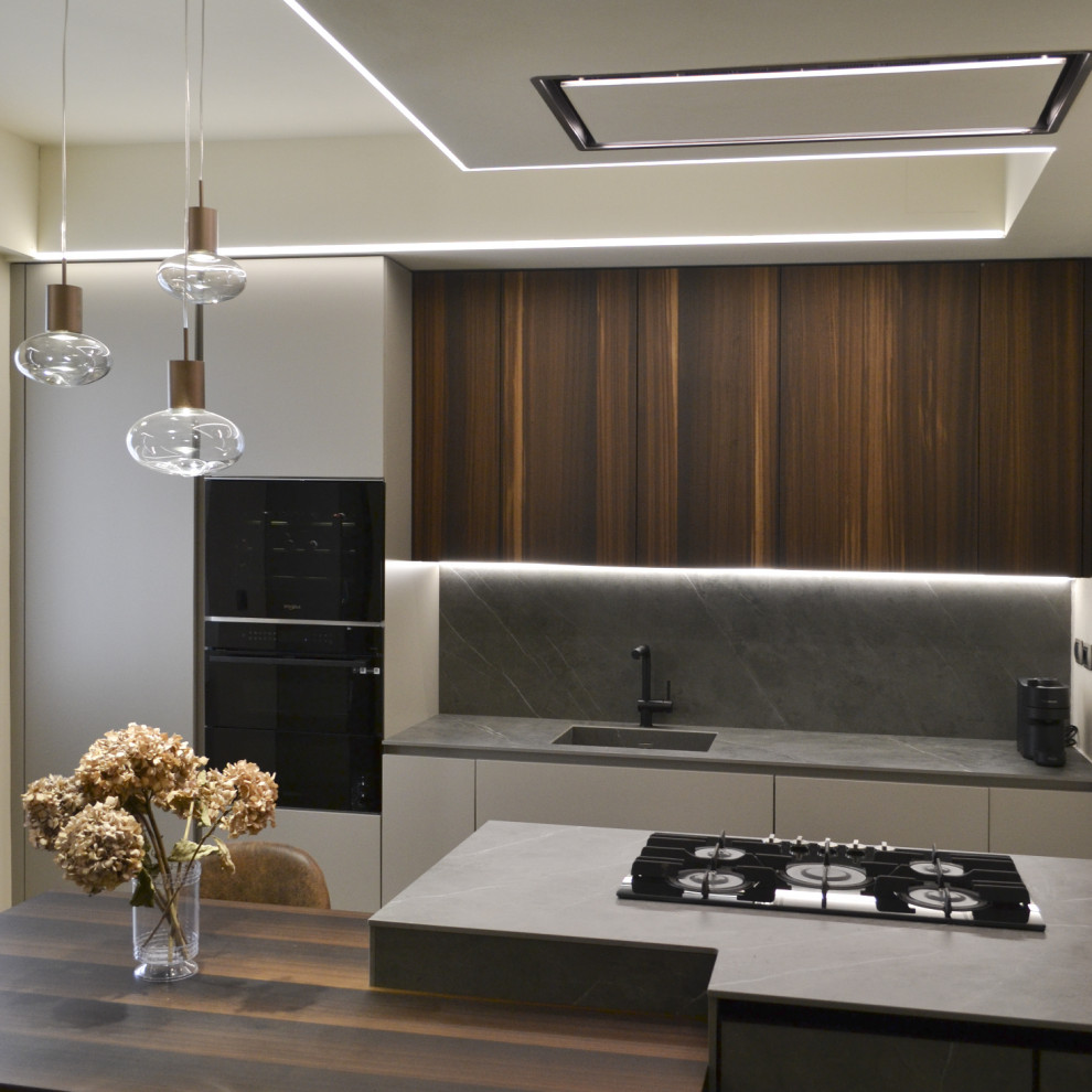 Photo of a medium sized contemporary single-wall open plan kitchen in Milan with an integrated sink, flat-panel cabinets, medium wood cabinets, marble worktops, grey splashback, marble splashback, black appliances, porcelain flooring, an island, beige floors, grey worktops and a drop ceiling.