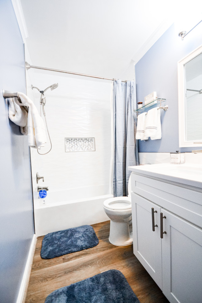 Cette image montre une petite salle de bain marine avec un placard à porte shaker, des portes de placard blanches, une baignoire posée, un combiné douche/baignoire, WC séparés, un carrelage blanc, des carreaux de céramique, un mur bleu, un sol en carrelage imitation parquet, un lavabo intégré, un plan de toilette en quartz modifié, un sol marron, une cabine de douche avec un rideau, un plan de toilette blanc, une niche, meuble simple vasque et meuble-lavabo encastré.