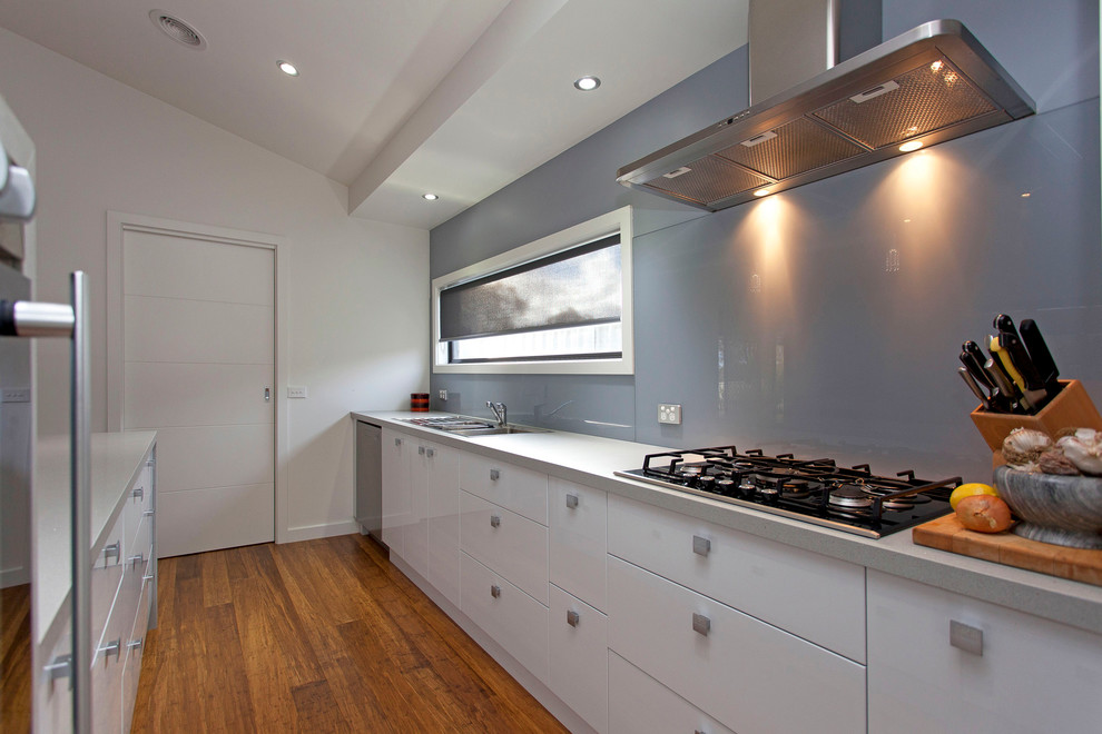 Photo of a mid-sized modern galley separate kitchen in Miami with a drop-in sink, flat-panel cabinets, white cabinets, recycled glass benchtops, grey splashback, stainless steel appliances, medium hardwood floors and with island.