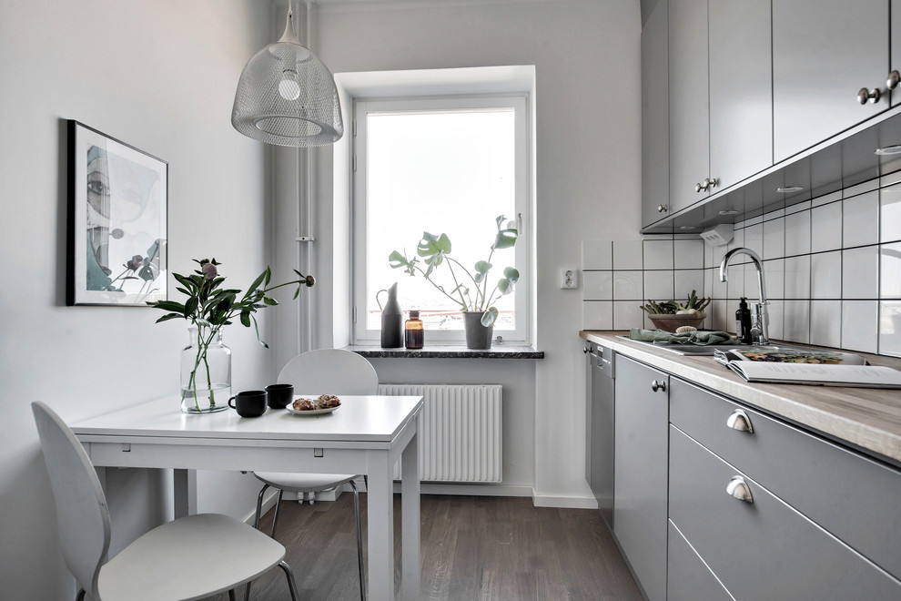 Small transitional single-wall separate kitchen in Gothenburg with dark hardwood floors, grey cabinets, wood benchtops, white splashback, ceramic splashback, stainless steel appliances, no island and brown floor.