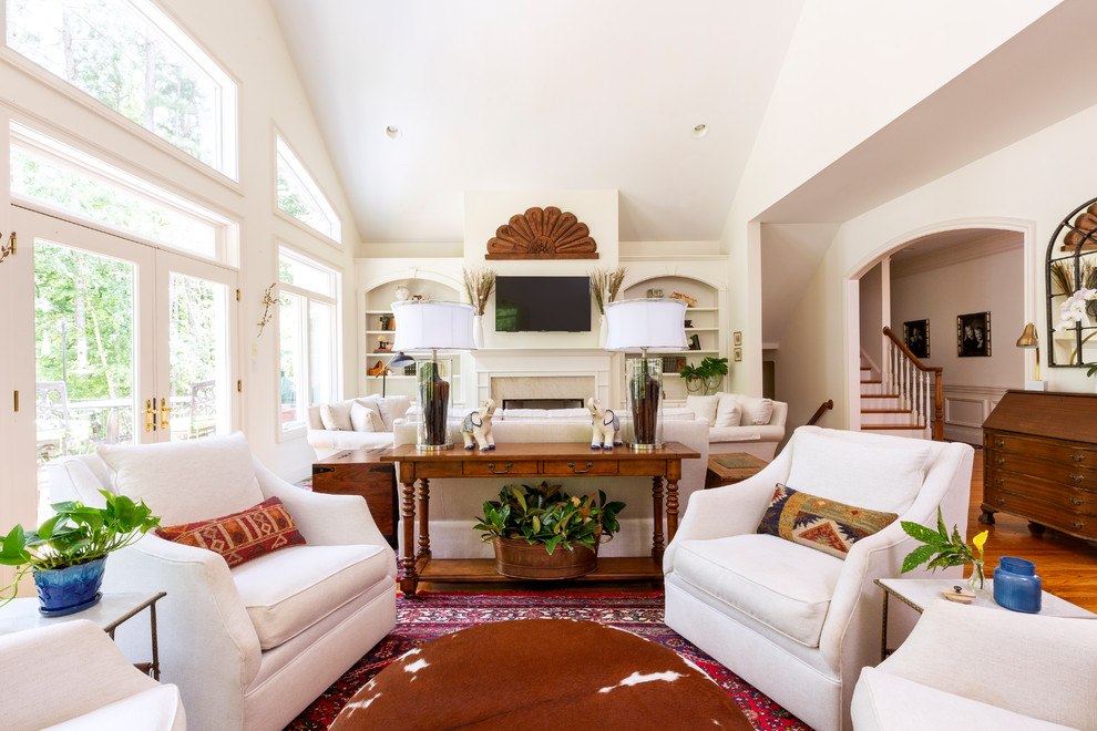 Design ideas for an expansive eclectic open concept living room in Charlotte with white walls, medium hardwood floors, a standard fireplace, a stone fireplace surround, a wall-mounted tv and brown floor.