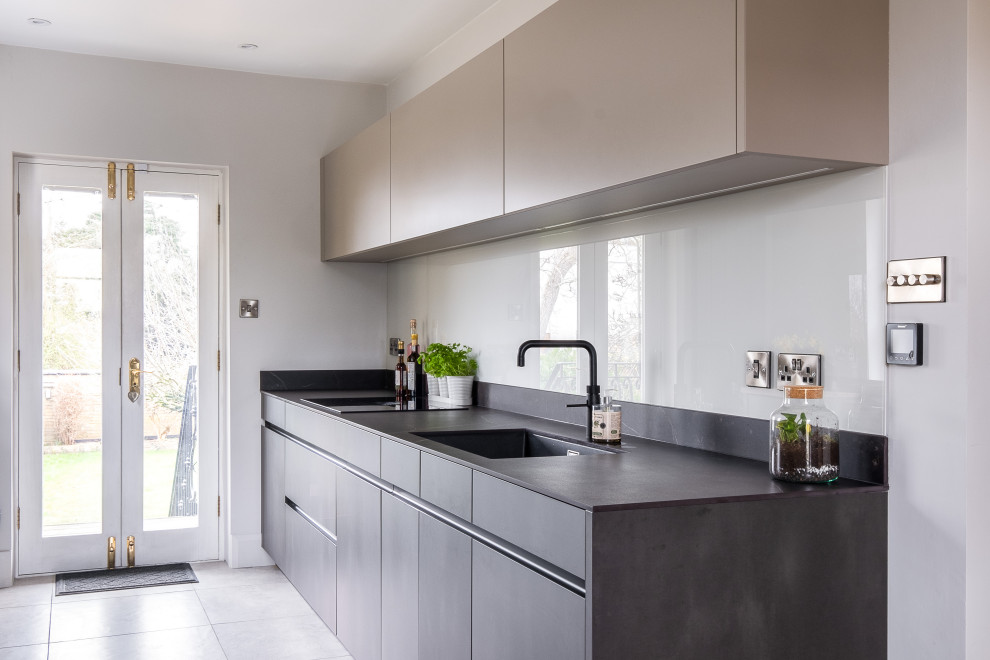 This is an example of a small contemporary galley enclosed kitchen in Gloucestershire with a built-in sink, flat-panel cabinets, composite countertops, black appliances, porcelain flooring, grey floors and black worktops.