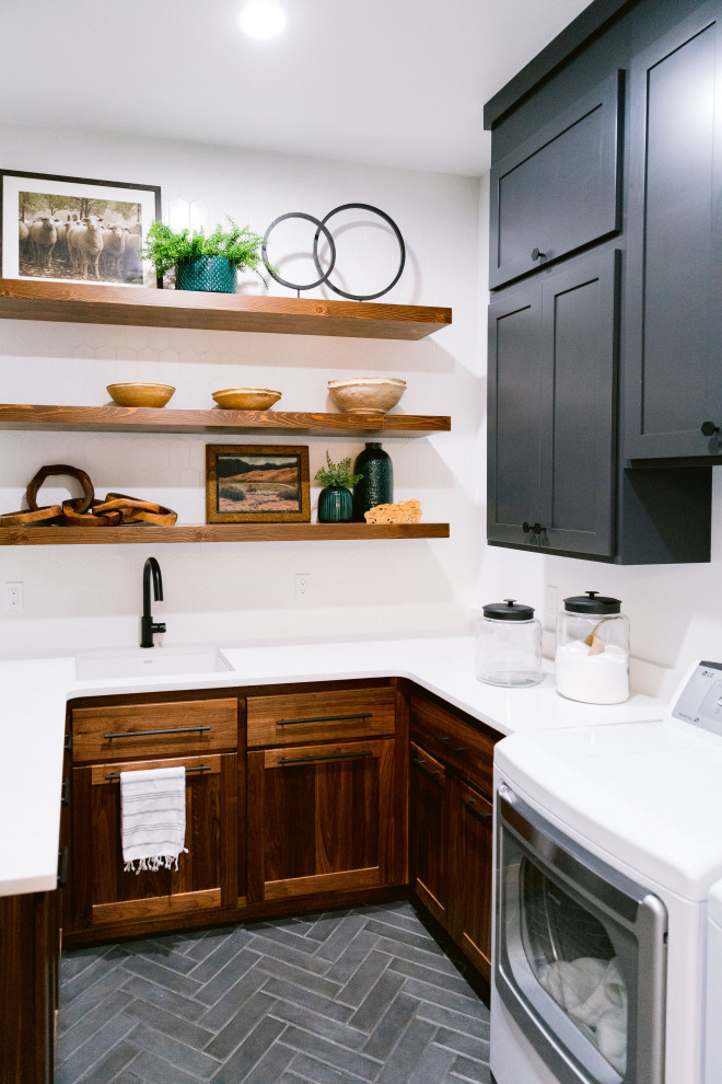 Inspiration for a country u-shaped laundry room in Boise with an undermount sink, dark wood cabinets, quartz benchtops, white splashback, ceramic splashback, white walls, ceramic floors, a side-by-side washer and dryer, grey floor and white benchtop.
