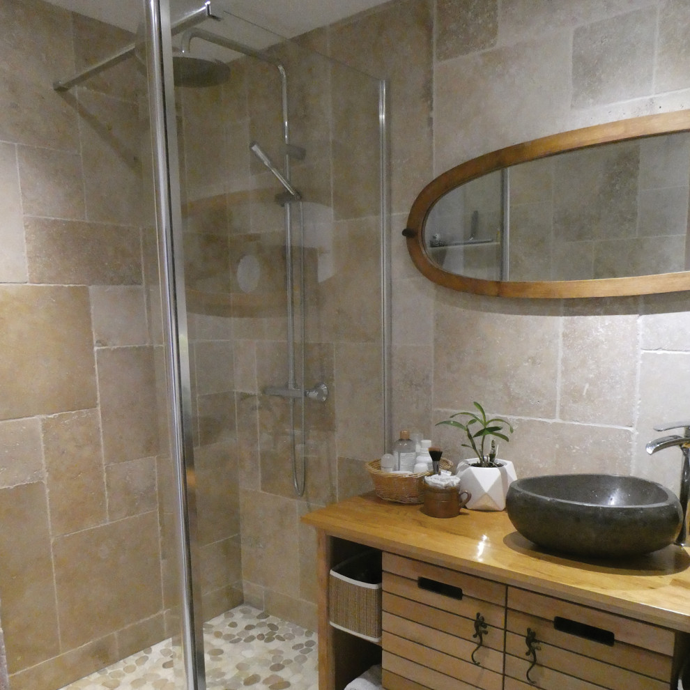 Foto på ett litet tropiskt brun badrum med dusch, med skåp i ljust trä, en kantlös dusch, beige kakel, travertinkakel, beige väggar, ett fristående handfat, träbänkskiva, grått golv och med dusch som är öppen