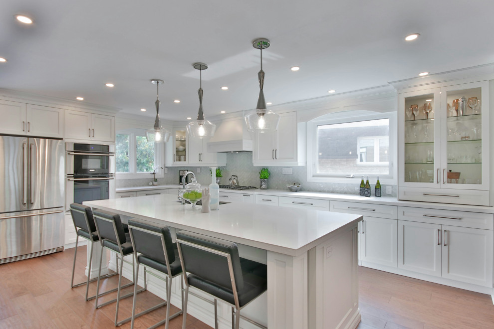 Classic l-shaped kitchen with a submerged sink, shaker cabinets, white cabinets, stainless steel appliances, medium hardwood flooring, an island, brown floors and white worktops.