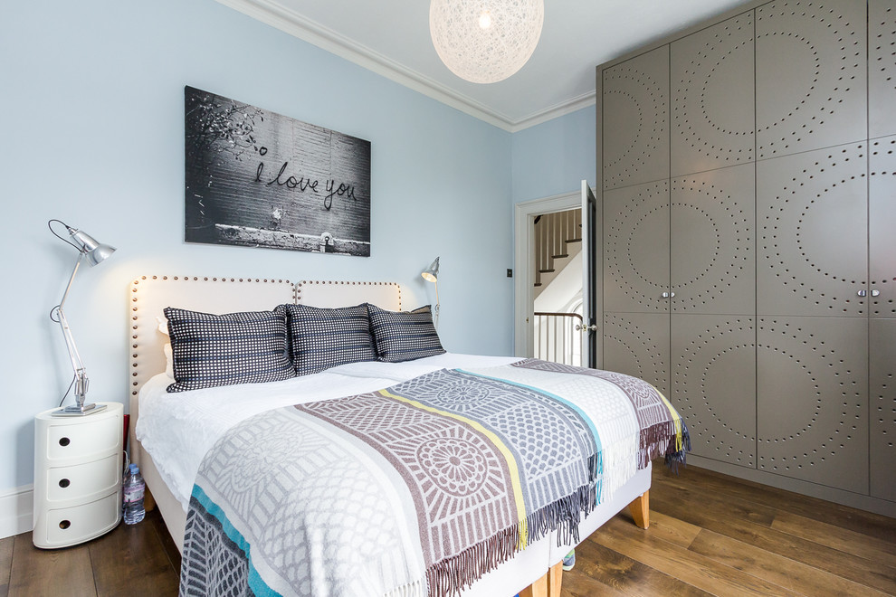 Photo of a transitional bedroom in London with blue walls and light hardwood floors.