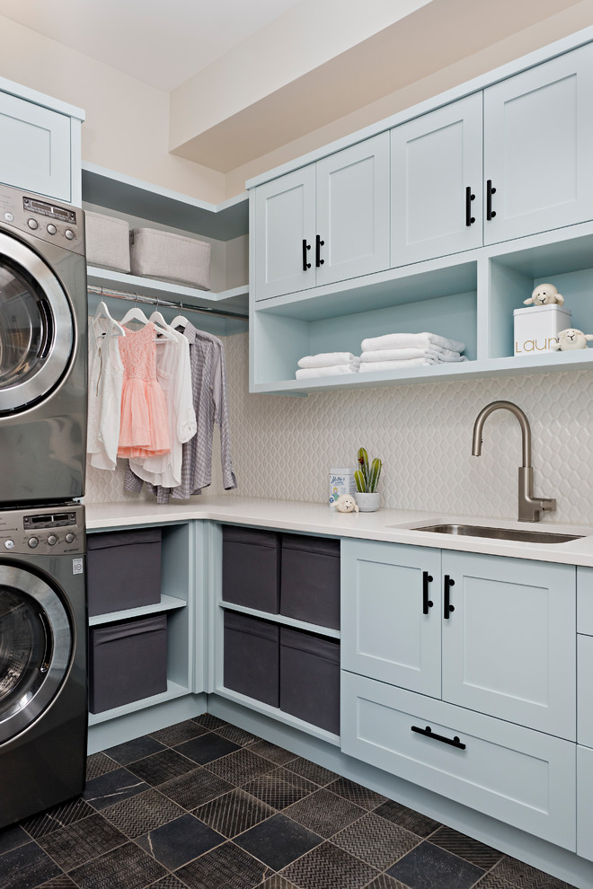 Photo of a country l-shaped dedicated laundry room in Toronto with an undermount sink, shaker cabinets, blue cabinets, a stacked washer and dryer, brown floor and white benchtop.