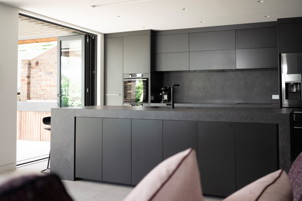 Inspiration for a mid-sized contemporary galley open plan kitchen in Sydney with an undermount sink, grey cabinets, solid surface benchtops, grey splashback, stone slab splashback, black appliances, cement tiles, with island, grey floor and grey benchtop.
