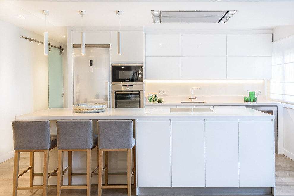 This is an example of a mid-sized modern l-shaped eat-in kitchen in Palma de Mallorca with an undermount sink, flat-panel cabinets, white cabinets, white splashback, stainless steel appliances and with island.