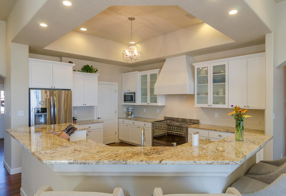 This is an example of a mid-sized l-shaped kitchen pantry in Albuquerque with an undermount sink, shaker cabinets, white cabinets, granite benchtops, beige splashback, glass sheet splashback, stainless steel appliances, with island and dark hardwood floors.