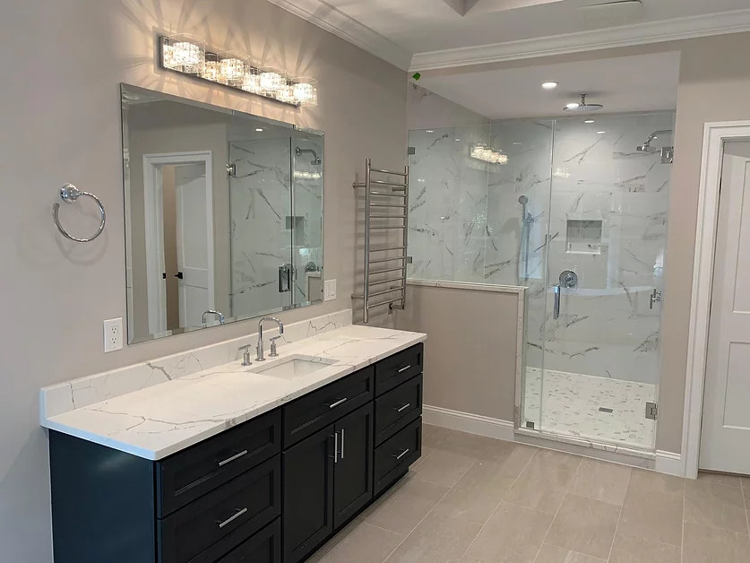 This is an example of a large modern grey and white ensuite bathroom in Raleigh with shaker cabinets, black cabinets, a freestanding bath, a double shower, a two-piece toilet, white tiles, porcelain tiles, grey walls, porcelain flooring, a submerged sink, engineered stone worktops, brown floors, a hinged door, white worktops, an enclosed toilet, double sinks and a built in vanity unit.