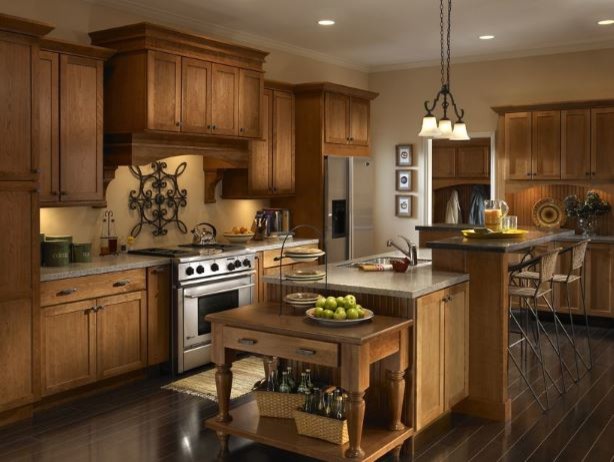 Example of a large classic l-shaped dark wood floor and brown floor eat-in kitchen design with a drop-in sink, recessed-panel cabinets, medium tone wood cabinets, granite countertops, beige backsplash, stone tile backsplash, stainless steel appliances and an island