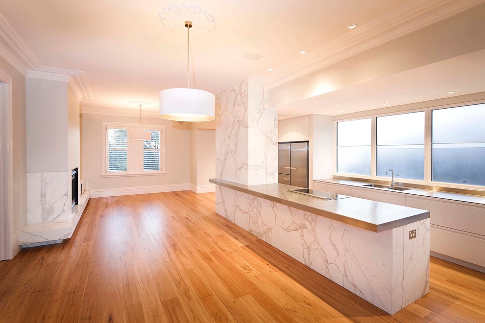 Photo of a contemporary u-shaped eat-in kitchen in Sydney with an undermount sink, flat-panel cabinets, white cabinets, stainless steel benchtops, stainless steel appliances, medium hardwood floors and with island.