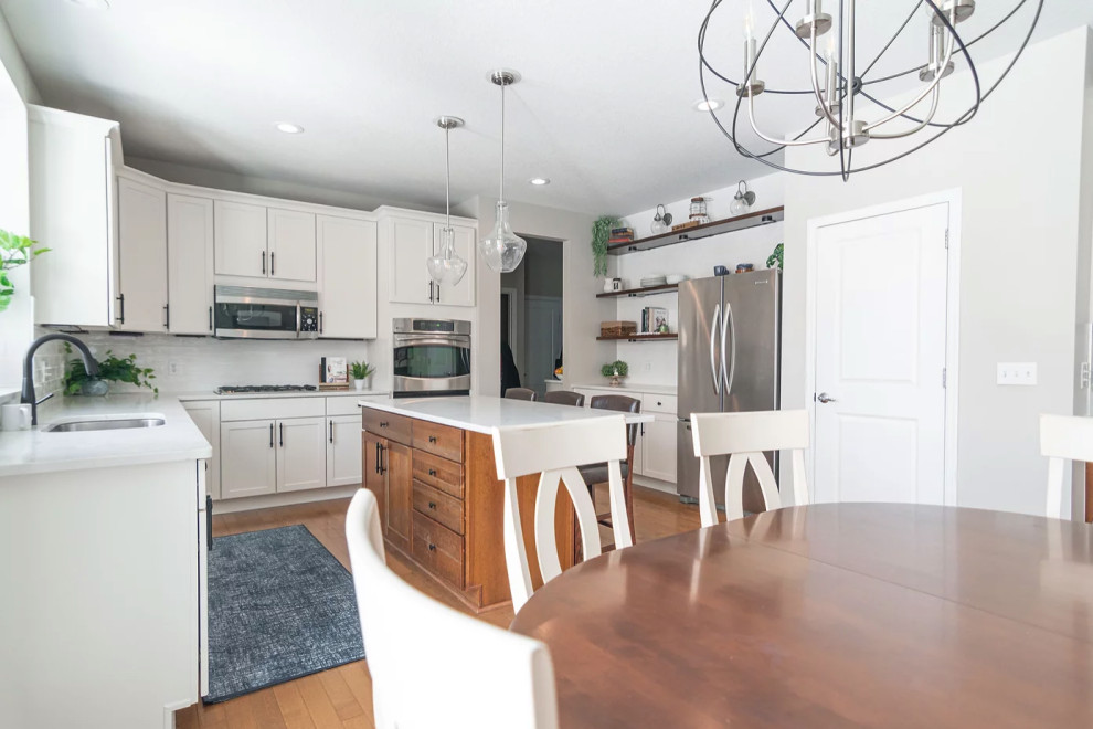 Large transitional u-shaped medium tone wood floor and brown floor eat-in kitchen photo in Minneapolis with a single-bowl sink, shaker cabinets, white cabinets, quartz countertops, white backsplash, porcelain backsplash, stainless steel appliances, an island and white countertops