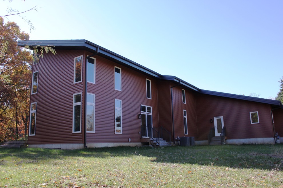 Modern two-storey red house exterior in St Louis with vinyl siding, a shed roof and a shingle roof.