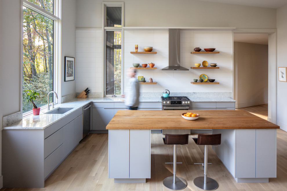 This is an example of a contemporary l-shaped kitchen in Other with an undermount sink, flat-panel cabinets, grey cabinets, wood benchtops, white splashback, stainless steel appliances, light hardwood floors, with island, beige floor and brown benchtop.