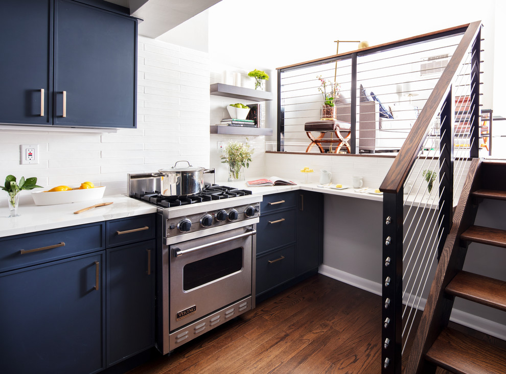 This is an example of a small transitional kitchen in New York with a farmhouse sink, blue cabinets, white splashback, ceramic splashback, coloured appliances, dark hardwood floors, no island and brown floor.