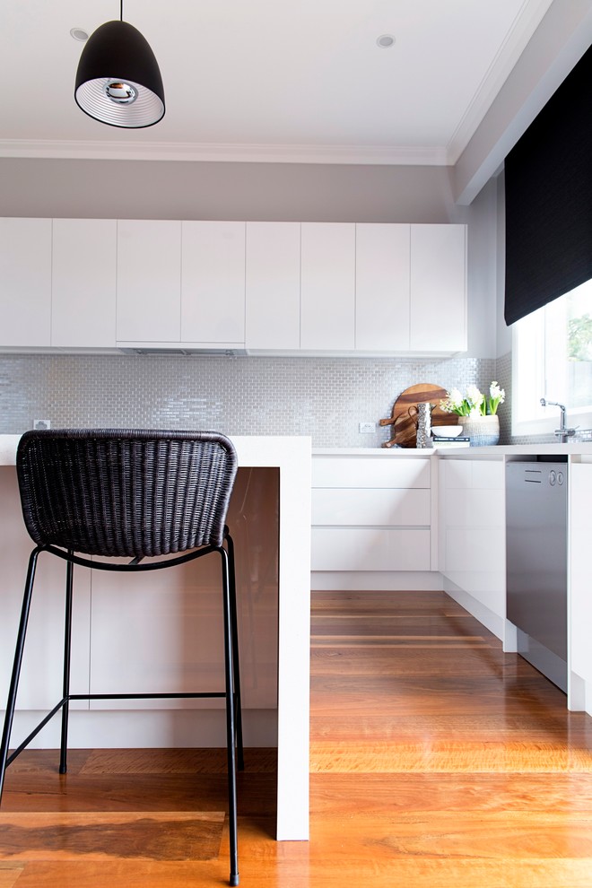 This is an example of a large contemporary u-shaped open plan kitchen in Melbourne with an undermount sink, white cabinets, quartz benchtops, metallic splashback, ceramic splashback, stainless steel appliances, light hardwood floors and with island.