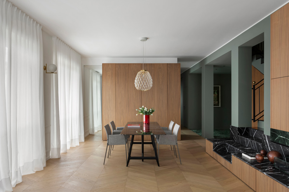 Offenes, Großes Modernes Esszimmer mit weißer Wandfarbe, braunem Holzboden, Tunnelkamin, Kaminumrandung aus Stein und vertäfelten Wänden in Mailand