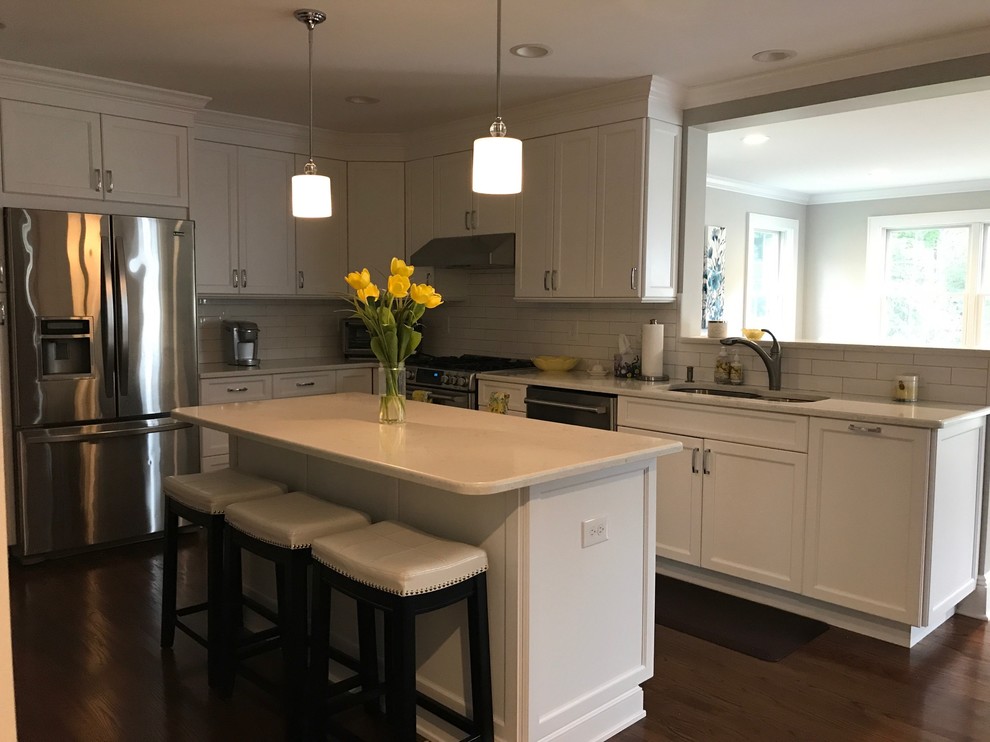 This is an example of a mid-sized transitional single-wall eat-in kitchen in New York with an undermount sink, shaker cabinets, white cabinets, granite benchtops, white splashback, subway tile splashback, stainless steel appliances, dark hardwood floors, with island and brown floor.