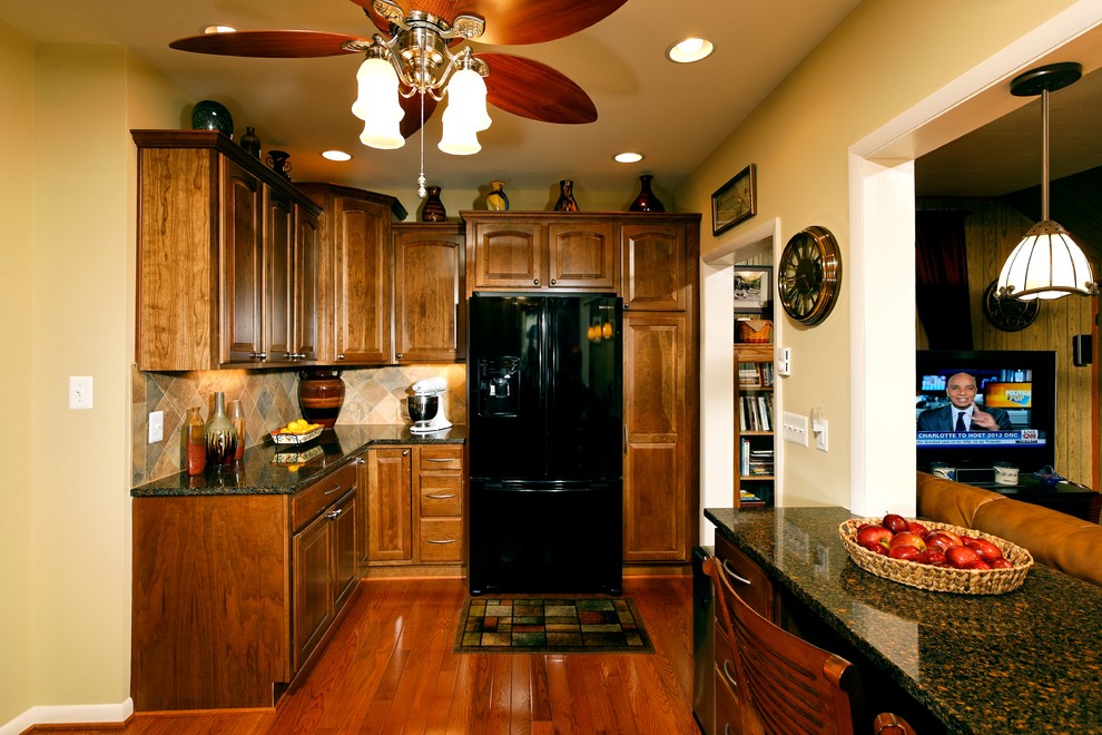 Example of a transitional l-shaped eat-in kitchen design in DC Metro with furniture-like cabinets, medium tone wood cabinets, granite countertops, beige backsplash, mosaic tile backsplash and black appliances