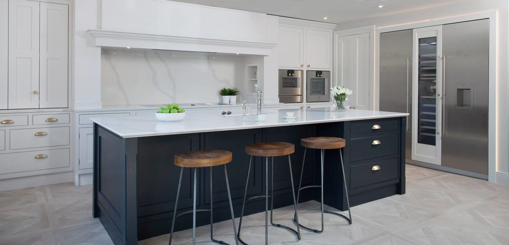 Design ideas for a mid-sized contemporary single-wall open plan kitchen in Belfast with an integrated sink, shaker cabinets, blue cabinets, solid surface benchtops, white splashback, marble splashback, stainless steel appliances, porcelain floors, with island, beige floor and white benchtop.