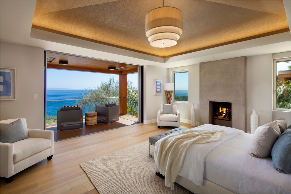 Large contemporary master bedroom in Santa Barbara with white walls, light hardwood floors, a standard fireplace and a concrete fireplace surround.
