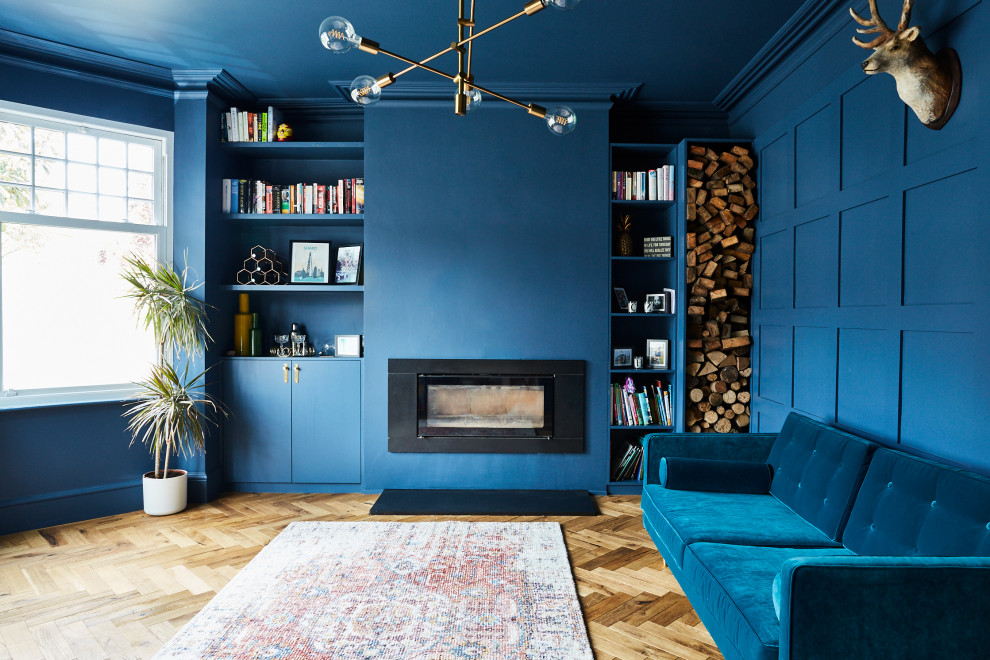 Modern inredning av ett stort separat vardagsrum, med blå väggar, mellanmörkt trägolv, en öppen vedspis och en spiselkrans i gips