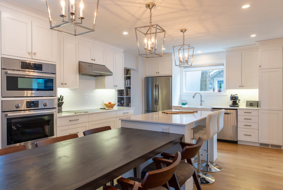 Inspiration for a large transitional l-shaped light wood floor eat-in kitchen remodel in Ottawa with a farmhouse sink, shaker cabinets, white cabinets, quartz countertops, white backsplash, porcelain backsplash, stainless steel appliances, an island and white countertops