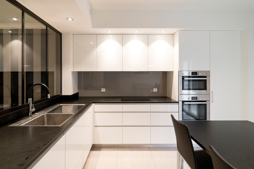 This is an example of a mid-sized contemporary l-shaped separate kitchen in Le Havre with a single-bowl sink, flat-panel cabinets, white cabinets, granite benchtops, grey splashback, panelled appliances, no island, beige floor and porcelain floors.