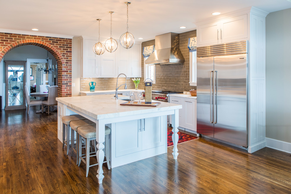 Open concept kitchen - mid-sized transitional l-shaped medium tone wood floor open concept kitchen idea in Other with shaker cabinets, white cabinets, gray backsplash, glass tile backsplash, stainless steel appliances, an island, a farmhouse sink and quartzite countertops