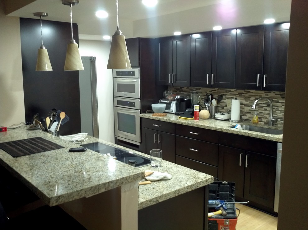 Photo of a mid-sized modern galley separate kitchen in Miami with an undermount sink, shaker cabinets, dark wood cabinets, granite benchtops, multi-coloured splashback, stainless steel appliances and bamboo floors.