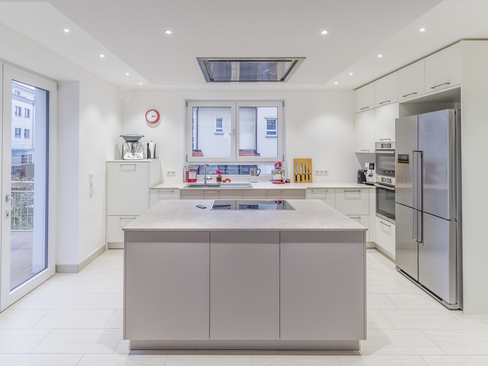 Photo of a mid-sized contemporary l-shaped open plan kitchen in Other with a drop-in sink, flat-panel cabinets, white cabinets, laminate benchtops, white splashback, stainless steel appliances, ceramic floors, with island, limestone splashback, beige floor and beige benchtop.